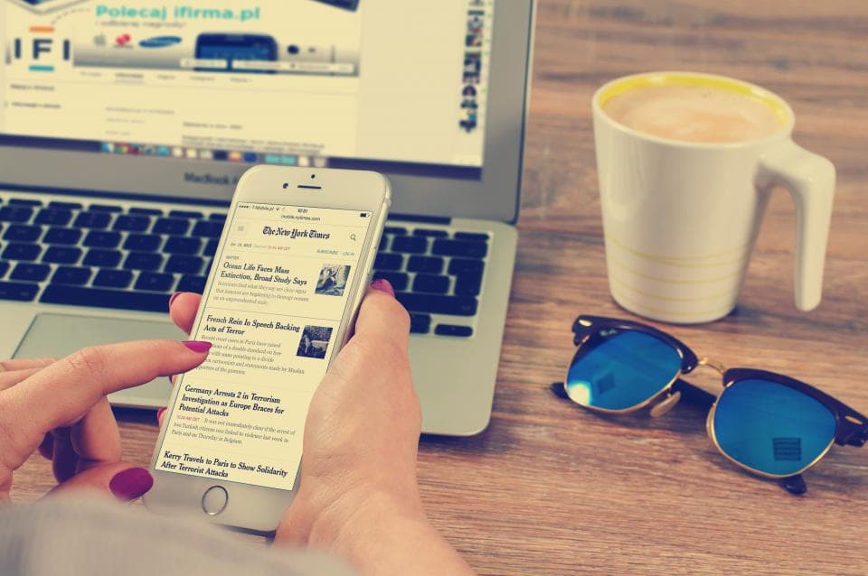 Person reading a mobile app on a phone beside a laptop and coffee