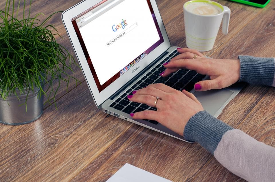 Person searching on Google on a laptop at a wooden desk
